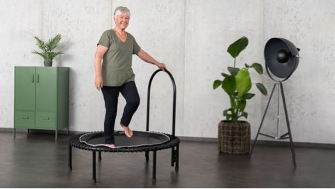 Woman standing on the health trampoline and holding onto the side support bar.