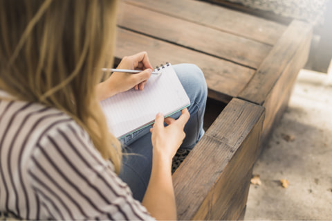 Woman sits on a bench and makes notes.
