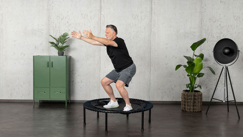 Un homme âgé s'entraîne sur le mini-trampoline bellicon et est en position accroupie.