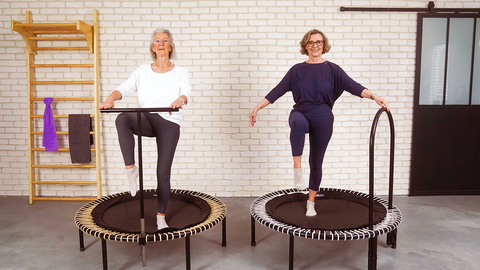 Deux dames âgées s'entraînent sur le mini-trampoline, l'une se tient à la barre en T, l'autre à la barre latérale.