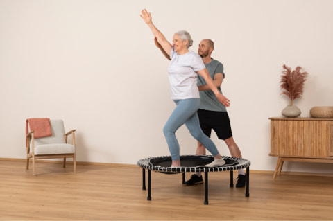 Woman standing on mini-trampoline being guided by man next to her during exercise.