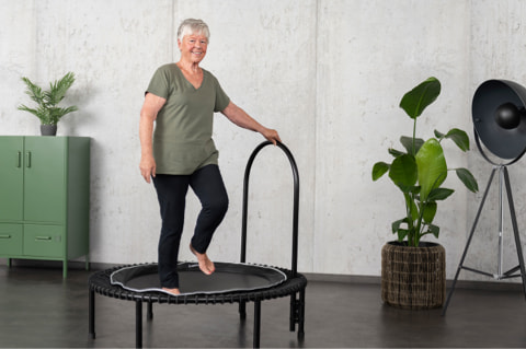 Older lady on bellicon mini trampoline with side support handle.